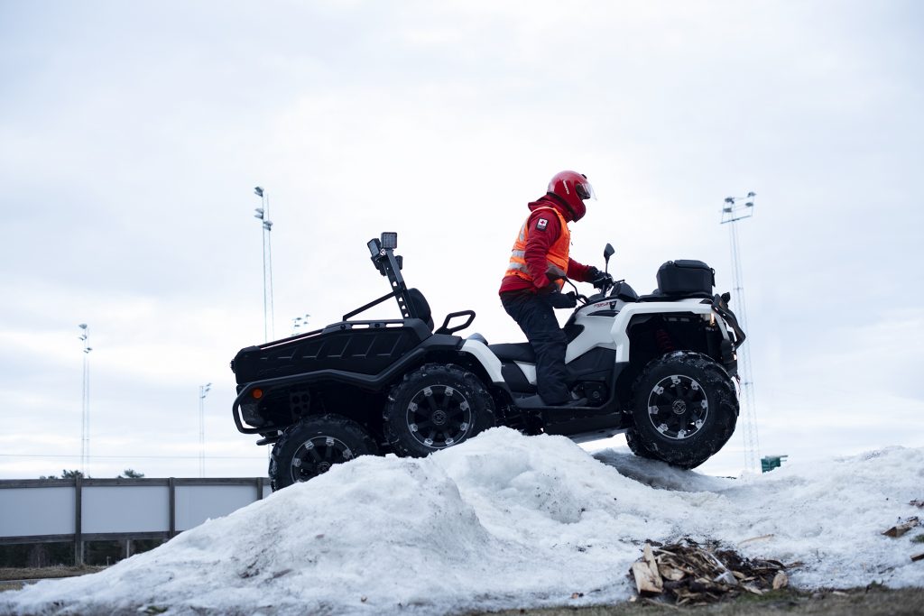 Mann fra hjelpekorpset kjører 6-hjuling på snøhaug. Det er overskya og våren er på vei.
Illustrasjon til påskeberedskapen.